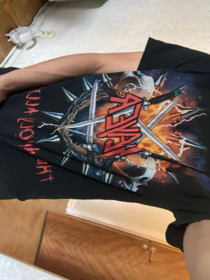 Slayer The Unholy Alliance t-shirt - Säljer en svart Slayer t-shirt med stort färgstarkt tryck fram. Motivet har bandets logga, eld, kedjor, svärd och dödskallar samt texten 'The Unholy Alliance' i rött. Perfekt för dig som gillar metal och vill sticka ut med en fet bandtröja. Lite för kort för mig, passar dig bra som är under 170 