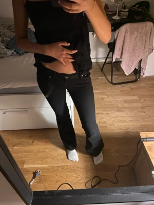 Svarta bootcut jeans - Säljer ett par svarta bootcut jeans med hög midja och klassisk femficksdesign. Jeansen har en snygg passform som sitter tajt upptill och släpper ut vid benen. Perfekta till en trendig vardagslook och passar till det mesta. Jag är 160 och de är lite korta på mig