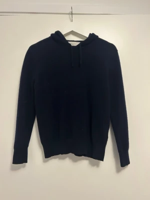 Mörkblå hoodie med huva - En enkel och stilren mörkblå hoodie med huva och dragssnören från Sayless clothing. Materialet är kaschmir så perfekt för kalla kvällar för den håller dig varm. Passar dig som gillar en clean och klassisk look. Nypris ligger på 999kr och är deras minsta storlek xxs men om ni har funderingar över produkten skriv det. Har ett litet hål vid vänstra ärmen men inget man märker.