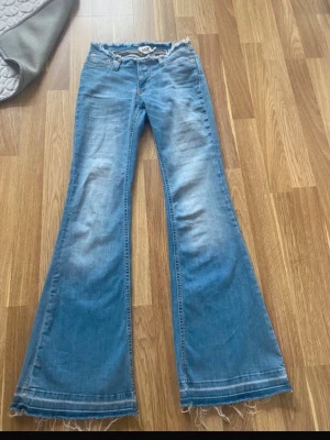 Blå utsvängda jeans med rå kant - Säljer ett par blå jeans med utsvängda ben och råa, fransiga kanter nertill. Dragkedjan fungerar utmärkt men den man drar upp med gick av. Short length 