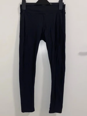 Svarta klassiska leggings - Ett par svarta, enkla leggings med hög midja och smal passform. De är helsvarta utan synliga detaljer eller mönster, perfekta till många olika outfits. Materialet ser stretchigt och bekvämt ut, vilket gör dem lätta att bära hela dagen.