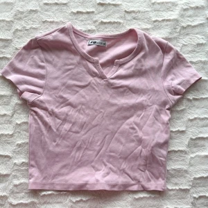 Ljusrosa croppad topp - Söt ljusrosa croppad topp med korta ärmar och en liten v-ringning framtill. Perfekt till jeans eller kjol för en chill och trendig look. Tillverkad i mjuk bomull som känns skön mot huden.