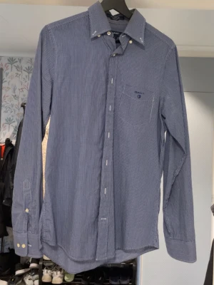 Blårutig skjorta från Gant - Klassisk blårutig skjorta från Gant med button-down krage och bröstficka med broderad logga. Skjortan har långa ärmar och vita knappar framtill samt vid ärmsluten. Perfekt till jeans eller chinos för en clean look.