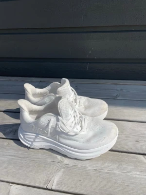 Vita Hoka One One Clifton 10 sneakers - Säljer ett par vita Hoka One One Clifton 10 sneakers med chunky sula och ventilerande mesh-ovandel. Skorna har klassisk snörning och en sportig, modern look som passar perfekt till streetwear eller träning. Nypris är 2099kr och dessa är i mycket fint skick! 