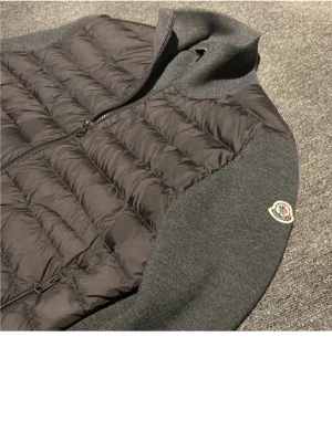 Grå pufferjacka med stickade ärmar - Snygg grå pufferjacka från Moncler med quiltad front och stickade ärmar. Jackan har hög krage, dragkedja framtill och Moncler-logga på ärmen. Perfekt för kalla vinterdagar och ger en stilren look.