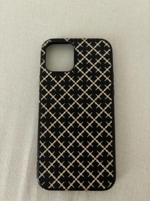 Svart mobilskal By Malene Birger - Snyggt svart mobilskal från By Malene Birger med beige grafiskt mönster. Skalets yta är slät och det är gjort i tåligt plastmaterial. Passar perfekt för dig som vill ha en stilren och trendig look till mobilen. Tyvärr vet ja inte exakt vilken modell den är till men den är lite trång på min iPhone 15 så antar att de är till en iPhone 13/14. Aldrig använd 