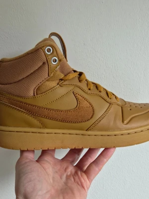 Nike Court Borough Mid 2 - Snygga high top sneakers från Nike i en brun färg med matchande snörning. Skorna har en kombination av läder och textilmaterial, med klassisk swoosh på sidan och perforerad tå för extra ventilation. Perfekta för dig som gillar streetstyle och vill sticka ut.