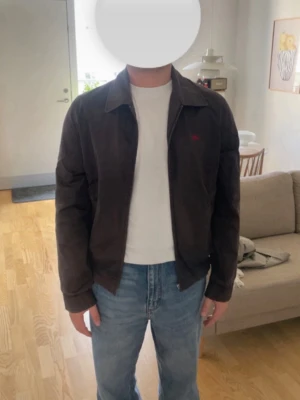 Burberry harrington jacka - Säljer en mörkbrun jacka från Burberry med klassiskt rutigt foder. Jackan har dragkedja framtill, normal passform och långa ärmar. Perfekt för dig som vill ha en stilren och tidlös look.