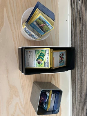Stor samling Pokémonkort i boxar - Säljer en stor samling Pokémonkort i olika boxar och burkar. Korten har gul ram och varierande motiv, inklusive energikort och olika Pokémon. Perfekt för samlare eller dig som vill bygga din egen lek. Boxarna är i plast och metall.