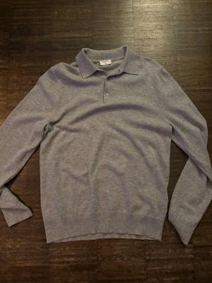 Ljusgrå stickad tröja från Filippa K - Snygg ljusgrå stickad tröja från Filippa K med klassisk krage och knäppning framtill. Tröjan har lång ärm och är tillverkad i mjukt, tunt material som passar perfekt för lager på lager. Enkel och stilren design som funkar till det mesta.