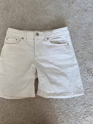 Vita jeansshorts - Snygga vita shorts i klassisk femficksmodell med knapp och dragkedja framtill. Shortsens midja är midwaist. Perfekta för varma dagar och enkla att matcha med olika stilar.