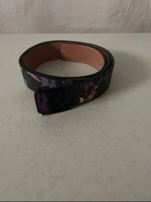 Svart bälte med färgglatt mönster - Snyggt svart bälte med färgglada detaljer och ett diskret mönster. Bältet har en stilren spänne och insida i beige. Perfekt accessoar för att lyfta din outfit.