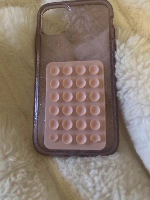 iPhone 11 mobilskal - Jag säljer ett lila glittrigt mobilskal för iPhone 11. Det har även en rosa silikonsugpropp som fastnar på till exempel en vägg. Jag har fått en ny telefon och säljer därför detta 💋🤞