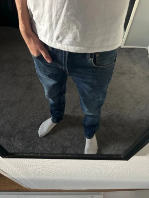 Jeans med slitningar - Säljer ett par klassiska blå jeans med rak passform och fem fickor. Jeansen har normal midja och snygga kontrastsömmar. Perfekta till vardags och passar till det mesta. Materialet är slitstark denim i bomull.