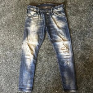 Blå slitna jeans - Säljer ett par blå  jeans med slitningar och tvättade detaljer. Jeansen har fem fickor, knappgylf och en klassisk passform. Perfekta för en avslappnad och trendig look.