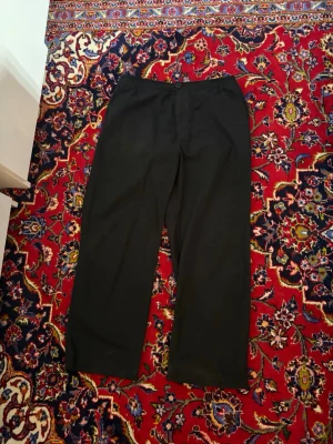 Svarta vida byxor från Weekday - Säljer ett par svarta byxor från Weekday med rak och vid passform. Byxorna har enkel design utan synliga detaljer och är tillverkade i ett mjukt tyg som känns bekvämt. Perfekta för dig som gillar minimalistisk stil.