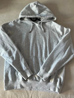Ljusgrå hoodie från 157 - Ljusgrå hoodie från 157 med klassisk huva och dragsnören, ribbade muddar vid ärmslut och nederkant. Perfekt för en avslappnad och stilren look.