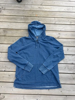 Blå hoodie med snörning - Säljer en blå hoodie med huva och snörning framtill. Hoodien har långa ärmar, känguruficka och är gjord i mjukt bomullsliknande material. Perfekt för chill dagar eller när du vill ha en avslappnad stil.