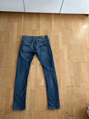 Nudie jeans - Säljer ett par klassiska blå jeans med raka ben och två bakfickor med vågformad söm. Jeansen har normal midja och bälteshällor. Perfekta till en avslappnad stil och passar till det mesta. Materialet är denim i bomull.