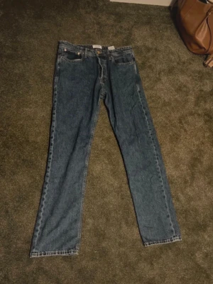 Blå raka jeans med hög midja - Klassiska blå jeans med rak passform och hög midja. Jeansen har fem fickor och stängs med dragkedja och knapp. Materialet är robust denim i bomull. Perfekta för en avslappnad och tidlös stil.