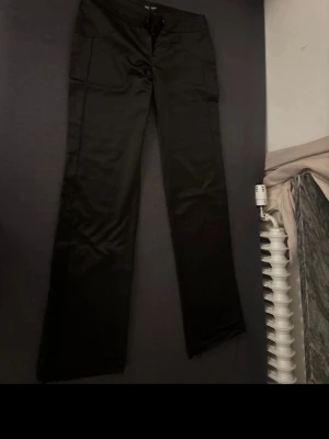 Svarta kostymbyxor från Alirfashion - Snygga svarta kostymbyxor från Alibifashion med raka ben och hög midja. Byxorna har diskret dragkedja och knapp framtill. Tillverkade i ett slätt tyg som ger en stilren look. Perfekta för dig som vill ha en clean och klassisk stil. Pris kan diskuteras 