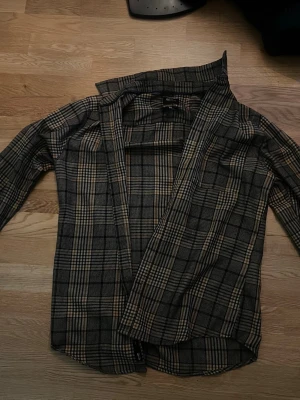 Rutig skjorta från Only & Sons - Säljer en snygg rutig skjorta från Only & Sons i slim fit. Skjortan har långa ärmar och klassisk krage. Färgerna går i mörkgrått, beige och svart, vilket ger en stilren look. Perfekt att matcha med jeans eller chinos.