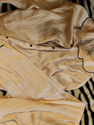 Ljusrosa satinpyjamas med svarta detaljer - Ett ljusrosa satinpyjamas sett med byxor och tröja från hm