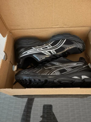 Acics - Snygga svarta sneakers med silvriga detaljer och meshpaneler för extra ventilation. Skorna har en chunky sula och sportig design med tydliga linjer på sidan. Perfekta för dig som gillar streetwear och vill ha en bekväm och trendig look. Kommer utan box frakta några andra skor med boxen