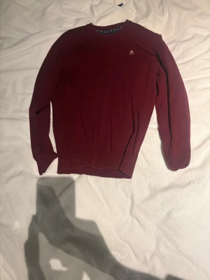 Vinröd tröja från Harper and Neyer - Snygg vinröd tröja från Harper and Neyer med rund halsringning och diskret logga på bröstet. Tröjan har långa ärmar och ribbade muddar vid ärmslut och nederkant. Perfekt för lager på lager och enkel att matcha med jeans.
