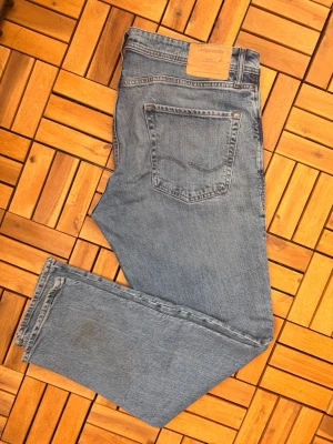 Blå raka jeans från Jack & Jones - Klassiska blå jeans från Jack & Jones i rak modell. Jeansen har fem fickor, normalhög midja och är tillverkade i slitstark denim. Perfekta för en avslappnad och tidlös stil. Priset för den behöver en tvätt, då det finns fläck nedre delen av benet som kommer gå bort i tvätten
