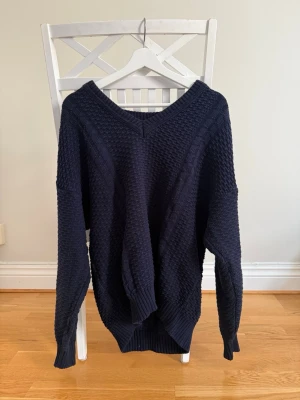 Mörkblå oversized stickad tröja - Mysig mörkblå stickad tröja med v-ringning och grovstickad struktur. Tröjan har långa ärmar, ribbade muddar och en avslappnad, oversized passform. Perfekt för lager på lager under kyliga dagar eller för en pluggkväll med vänner 🩷