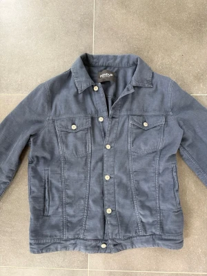 Mörkblå overshirt från Dondup - Snygg mörkblå overshirt från Dondup i mjukt bomullsmaterial. Klassisk jeansjacke-modell med två bröstfickor med lock och knappar, samt sidofickor. Rak passform och stilrena silvriga knappar framtill. Perfekt lager på lager-plagg för en avslappnad look. Skick: 9/10 | Storlek: 50 (M) Skicka meddelande för mer info eller bilder! Allt gott!