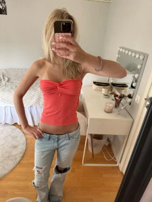 Korallfärgad tubtopp - Snygg korallfärgad tubtopp med twistad detalj framtill. Toppen är axelbandslös och croppad, perfekt till jeans eller kjol. Mjuk och stretchig bomullskänsla som sitter bekvämt mot kroppen.