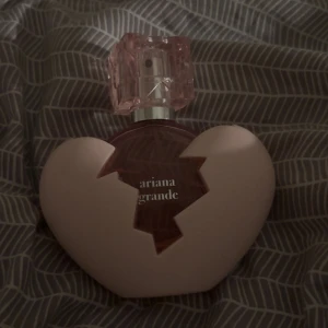 Ariana Grande parfym thank you next - Säljer en parfym från Ariana Grande med en unik hjärtformad flaska i ljusrosa och ett transparent rosa lock. Flaskan har en cool design med ett trasigt hjärta och text på framsidan. Perfekt för dig som gillar snygga och trendiga parfymer.