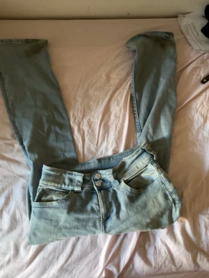 Ljusblå low waist washed jeans - Säljer ett par ljusblå low waist jeans med utsvängda ben och dubbla silverknappar i midjan. Jeansen har klassiska fem fickor och är gjorda i mjukt denimtyg. Perfekta för en avslappnad och trendig look. Dom är från barn avdelningen i storlek 170, dom passar mig som har på mig S. Dock är dom smutsiga vid där vid foten men det går att få bort via tvätt 