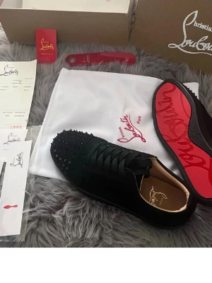 Louboutins  - Oanvända!! Snygga svarta sneakers från Christian Louboutin med mattsvarta nitar på tån och den ikoniska röda sulan. Skorna har en låg profil och är tillverkade i mocka med läderdetaljer. Perfekta för dig som vill sticka ut med exklusiv design.