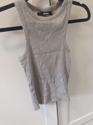 Grå ribbad linnetopp från Bik Bok - Enkel och stilren grå ribbad linnetopp från Bik Bok. Toppen är ärmlös med rund halsringning och har en tight passform. Perfekt att matcha med jeans eller kjol för en clean look.