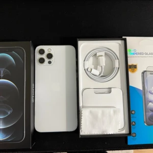 iPhone 12 Pro 128Gb | Nytt batteri 100% med nya tillbehör - Säljer en silverfärgad iPhone 12 Pro med stilren design, platt glasbaksida och ram i metall. Tre kameror på baksidan och Apple-logga. Medföljer laddkabel, putsduk och skärmskydd. Perfekt för dig som vill ha en snygg och kraftfull mobil.