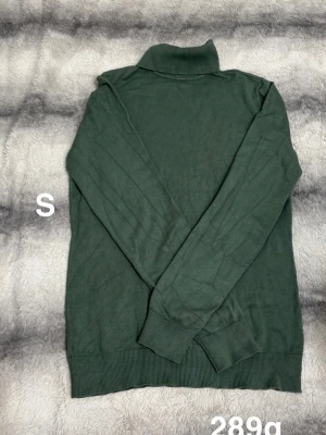 Mörkgrön polotröja - Stilren mörkgrön polotröja med lång ärm och ribbade muddar vid ärmslut och nederkant. Tröjan har en hög polokrage. material som känns skönt mot huden. Perfekt för dig som gillar enkel och klassisk design.🌸 Fint använt skick. Storlek s