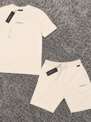 Beige set från Sonneti med t-shirt & shorts - Snyggt set från Sonneti i beige med matchande t-shirt och shorts. T-shirten har rund hals och diskret logga på bröstet. Shortsen har dragsko i midjan, fickor och samma stilrena logga. Perfekt för en avslappnad look. Materialet känns mjukt och bekvämt.