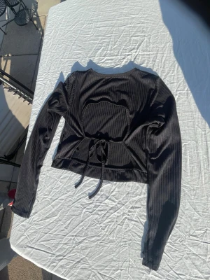 Svart snygg ribbad långärmad topp, strl M - Säljer min snygga gamla favorit topp som är en svart långärmad topp i ribbat tyg, som är öppen i ryggen och har knytning baktill. Är i storlek Medium. Den har en croppad passform och är perfekt en utekväll eller på en fin middag. Materialet känns mjukt och följsamt mot kroppen. Finns inga defekter på tröjan. Säljes tyvärr pga för liten🤩☺️