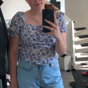 Blommig blus med puffärmar - Säljer en blommig blus i storlek S, som är vit och blå med puffiga kortärmar och knytning framtill vid bysten. Säljes pga för liten🤩☺️