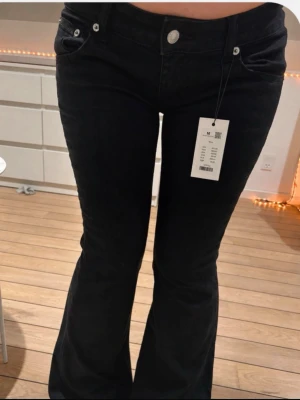 Svarta Blaze jeans  - Snygga svarta jeans med utsvängda ben och klassisk femficksmodell. Jeansen har låg midja och stängs med knapp och dragkedja. Perfekta för dig som gillar en trendig och bekväm stil.i modellen short