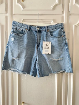 Ljusblå denimshorts - Ljusblå denimshorts från Stradivarius med slitna detaljer framtill. Hög midja och avslappnad passform. Helt oanvända med alla lappar kvar på! Nypris var 329kr 