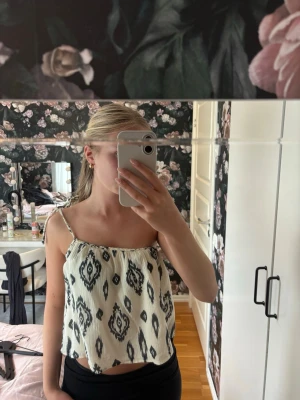 Beige och svart mönstrad linnetopp - Säljer en superfin luftig linnetopp med smala axelband och svart grafiskt mönster på beige botten. Toppen har en avslappnad passform och ett band som knyts på ena axeln. 🌸