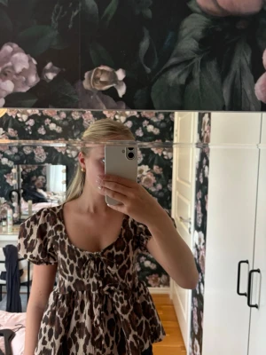 Leopardmönstrad blus med puffärm - Snygg blus från Gina Tricot med leopardmönster i brunt och beige. Modellen har puffiga korta ärmar, djup urringning och knytning framtill. Tillverkad i ett mjukt, stretchigt material som ger en bekväm passform. Perfekt för att lyfta vilken outfit som helst.🌸