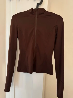 Brun ziptröja med hög krage - Snygg brun ziptröja med hög krage och figurnära passform. Tröjan har långa ärmar och dragkedja framtill. Perfekt till lager på lager och enkel att matcha med olika outfits.