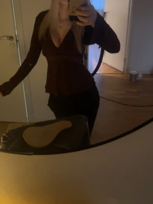 Vinröd v-ringad blus - Snygg mörkbrun blus med djup v-ringning och långa ärmar. Blusen har en figurnära passform och markerad midja som ger en feminin siluett. Perfekt att styla med både jeans och kjol.