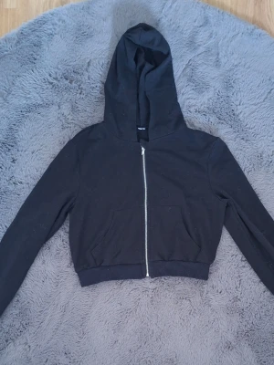 3 stycken croppade hoodies med dragkedja - Tre croppade hoodies i svart, vitt och grå med dragkedja framtill och stora fickor på magen. Alla har huva och långa ärmar. Perfekta för en chill och avslappnad stil. Materialet känns mjukt och bekvämt, troligen bomull eller bomullsblandning.