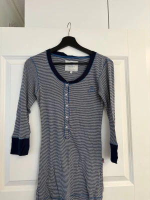 Randig pyjamas från Lexington - Mysig långärmad pyjamas från Lexington i marinblått och vitt med tunna ränder. Modellen har knappar framtill, rund halsringning och kontrastfärgade muddar vid ärmslut och hals. 
